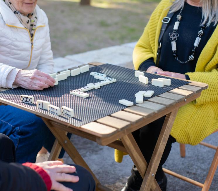 osoby siedzą na świeżym powietrzu przy stole grają w domino