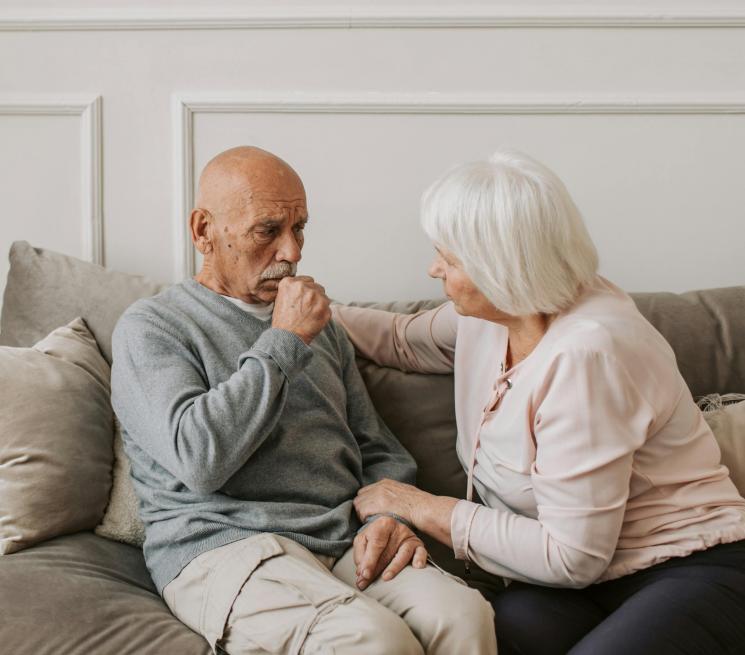 para seniorów siedzi na kanapie mężczyzna kaszle kobieta go obejmuje