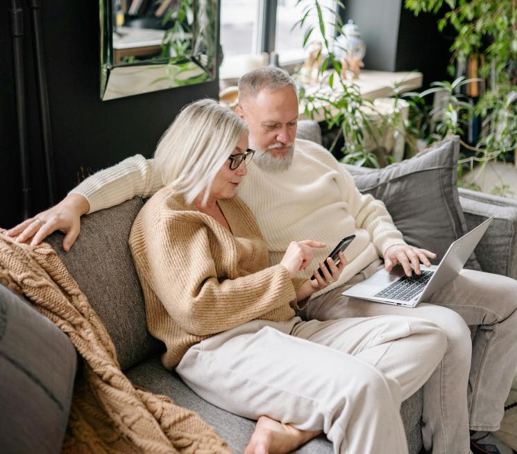 para seniorów siedzi na kanapie mężczyzna pracuje na laptopie kobieta patrzy na smartfon