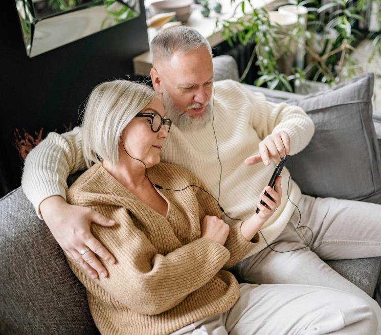 para seniorów siedzi na kanapie i słucha muzyki przez słuchawki na telefonie