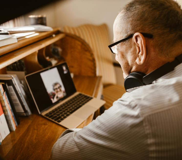 zdjęcie starszy mężczyzna z słuchawkami na szyi ogląda webinar lub prowadzi video rozmowę