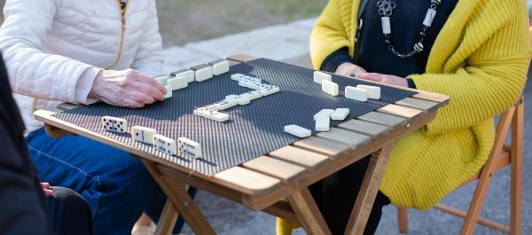 osoby siedzą na świeżym powietrzu przy stole grają w domino