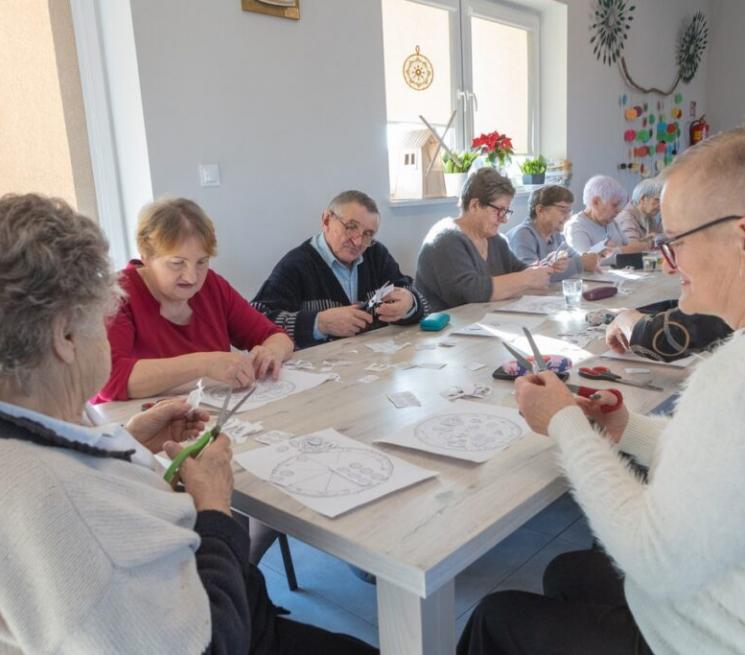 zdjęcie grupy seniorów siedzących przy stole i wykonujących prace plastyczne