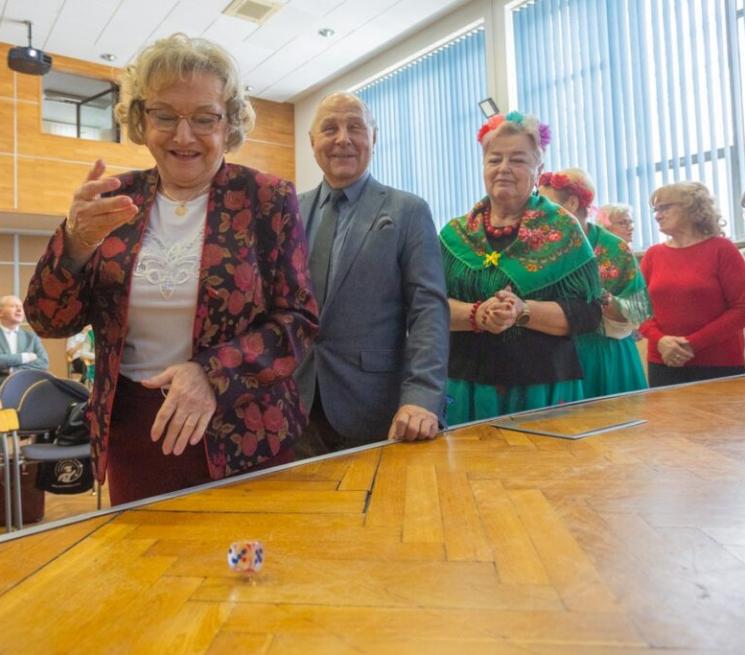 zdjęcie uśmiechnięci seniorzy stoją w kolejce do rzucenia kostką