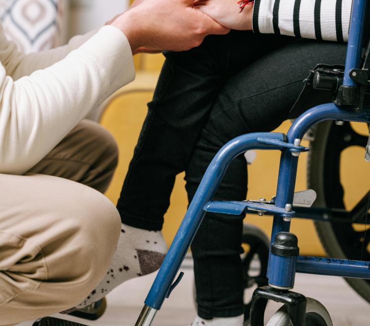 zdjęcie osoba kuca i trzyma za ręce kobietę siedzącą na wózku inwalidzkim