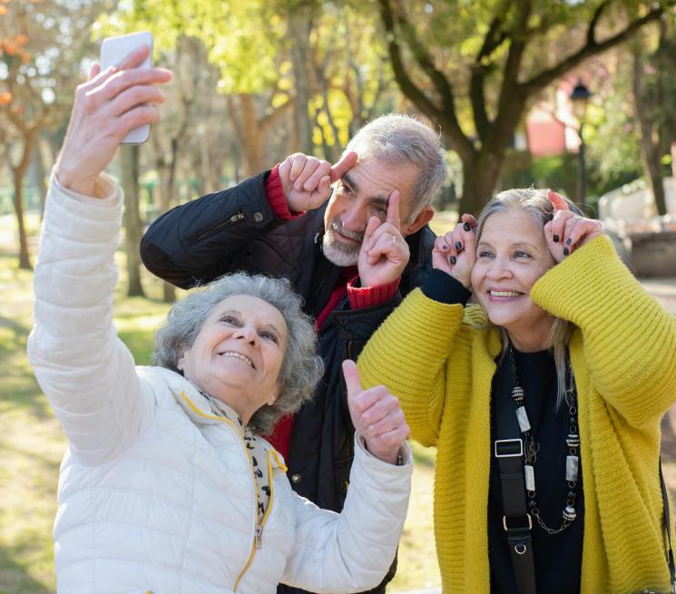 zdjęcie dwie seniorki i senior uśmiechają się do smartfonu i robią sobie zdjęcie w plenerze