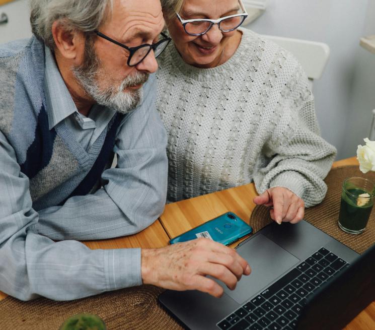 zdjęcie dwójka uśmiechniętych seniorów kobieta i mężczyzna pracują na laptopie