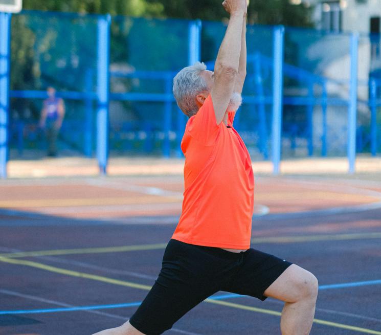 zdjęcie starszy mężczyzna w sporotywm ubraniu gimnastykuje sie na boisku