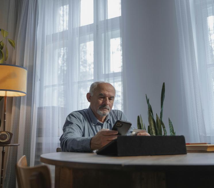 zdjęcie starszy mężczyzna siedzący przy stole patrzy w telefon
