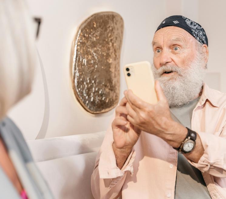 zdjęcie starszy mężczyzna z siwą brodą i chustą na głowie robi zdjęcie smartfonem siedzącej obok starszej kobiecie