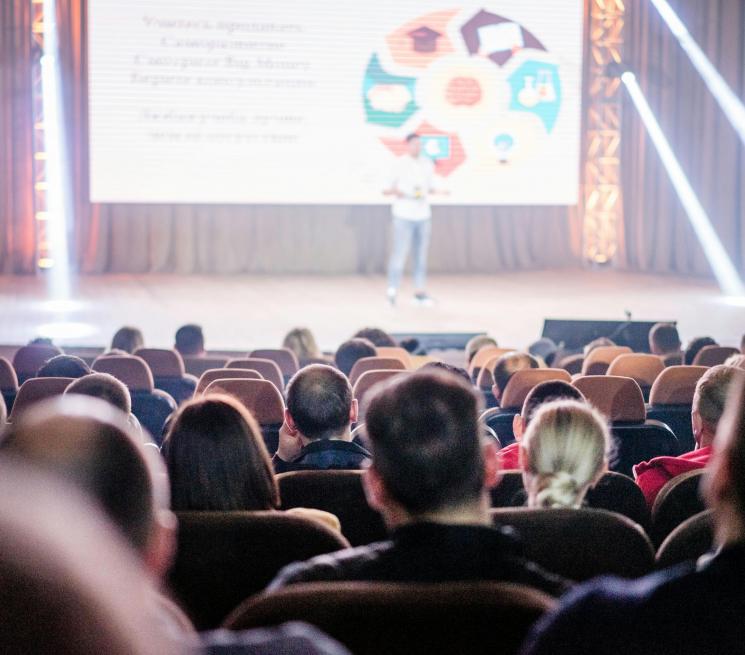 zdjęcie sala konferencyjna rząd krzeseł zdjęcie osób siedzących tyłem na scenie prelegent