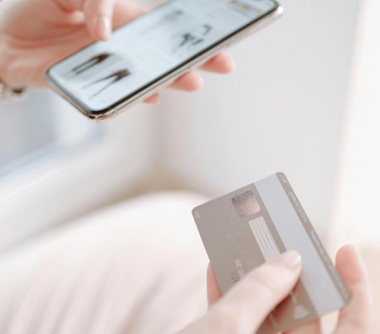 zdjęcie kobieta w jednej ręce trzyma telefon z aplikacją zakupową w drugiej kartę bakomatową