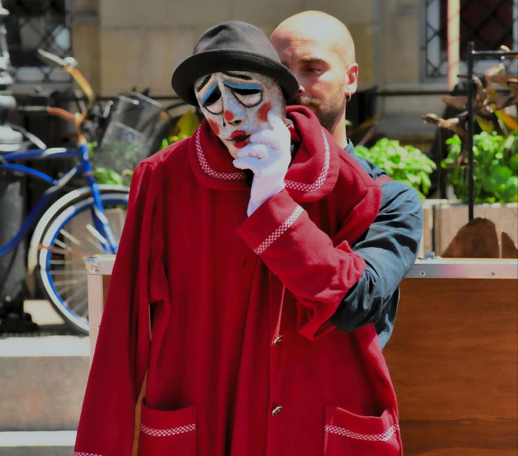 zdjęcie teatr uliczny mężczyna w czerwonym płaszczu w lewej dłoni w rękawiczce trzyma maskę w kapeluszu