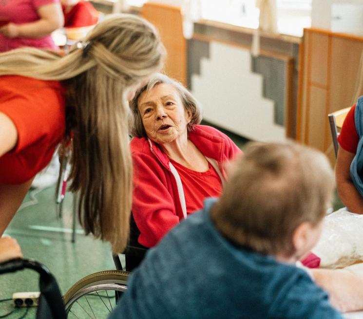 zdjęcie placówka dla seniorów opiekunka rozmawia z seniorką siedzącą na wózku inwalidzkim