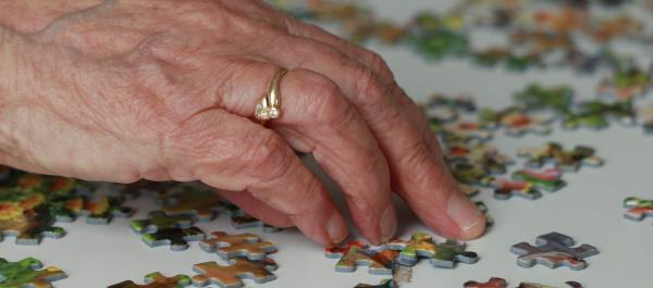 zdjęcie dłoni starszej kobiety układającej puzzle