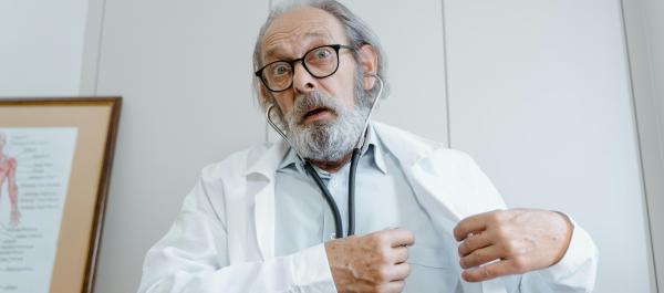 zdjęcie starszy mężczyna z siwą brodą w kitlu lekarskim i osłuchuje siebie stetoskopem