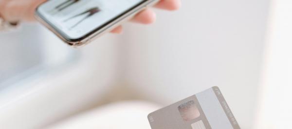 zdjęcie kobieta w jednej ręce trzyma telefon z aplikacją zakupową w drugiej kartę bakomatową