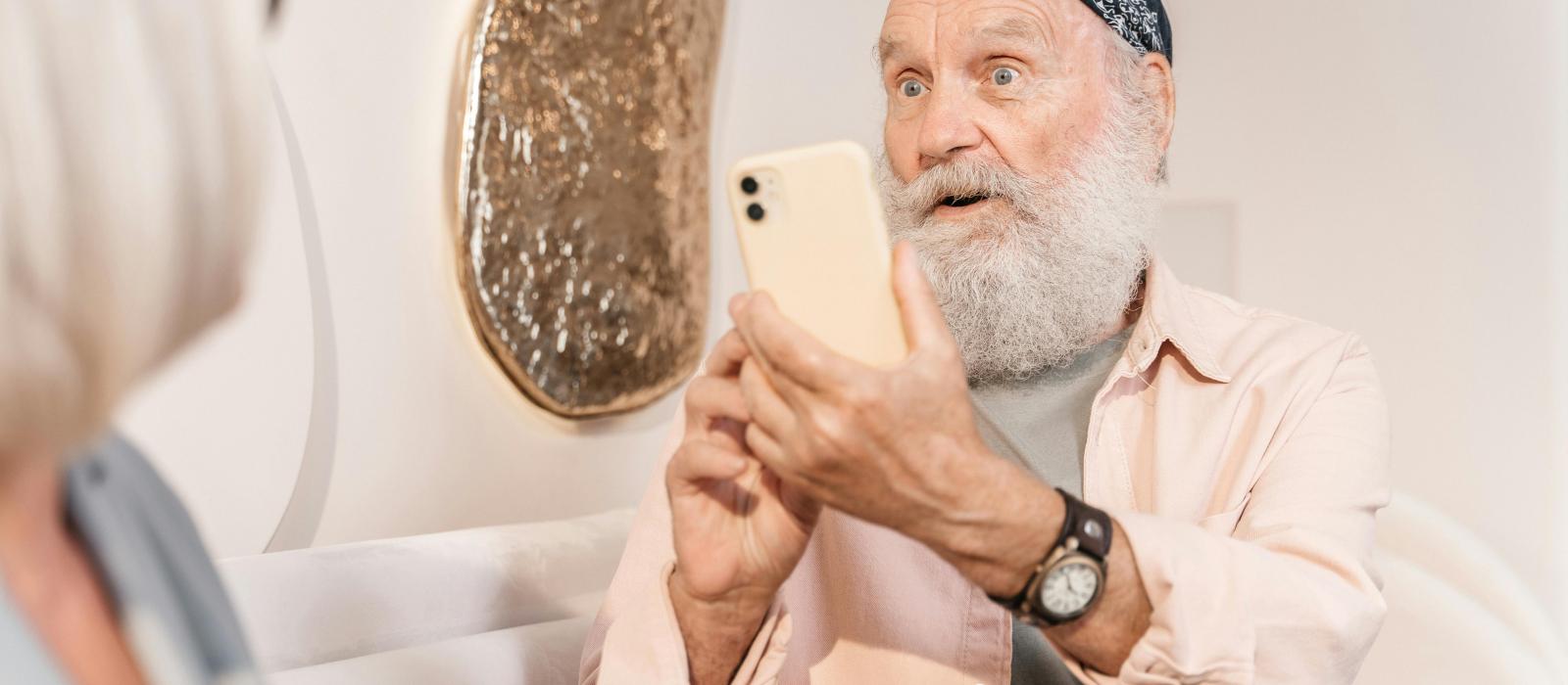 zdjęcie starszy mężczyzna z siwą brodą i chustą na głowie robi zdjęcie smartfonem siedzącej obok starszej kobiecie