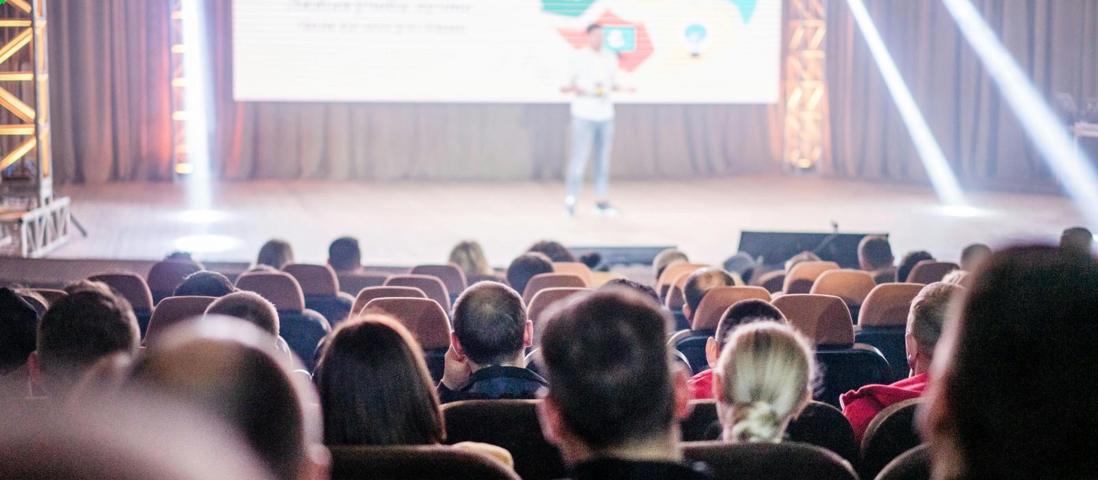 zdjęcie sala konferencyjna rząd krzeseł zdjęcie osób siedzących tyłem na scenie prelegent